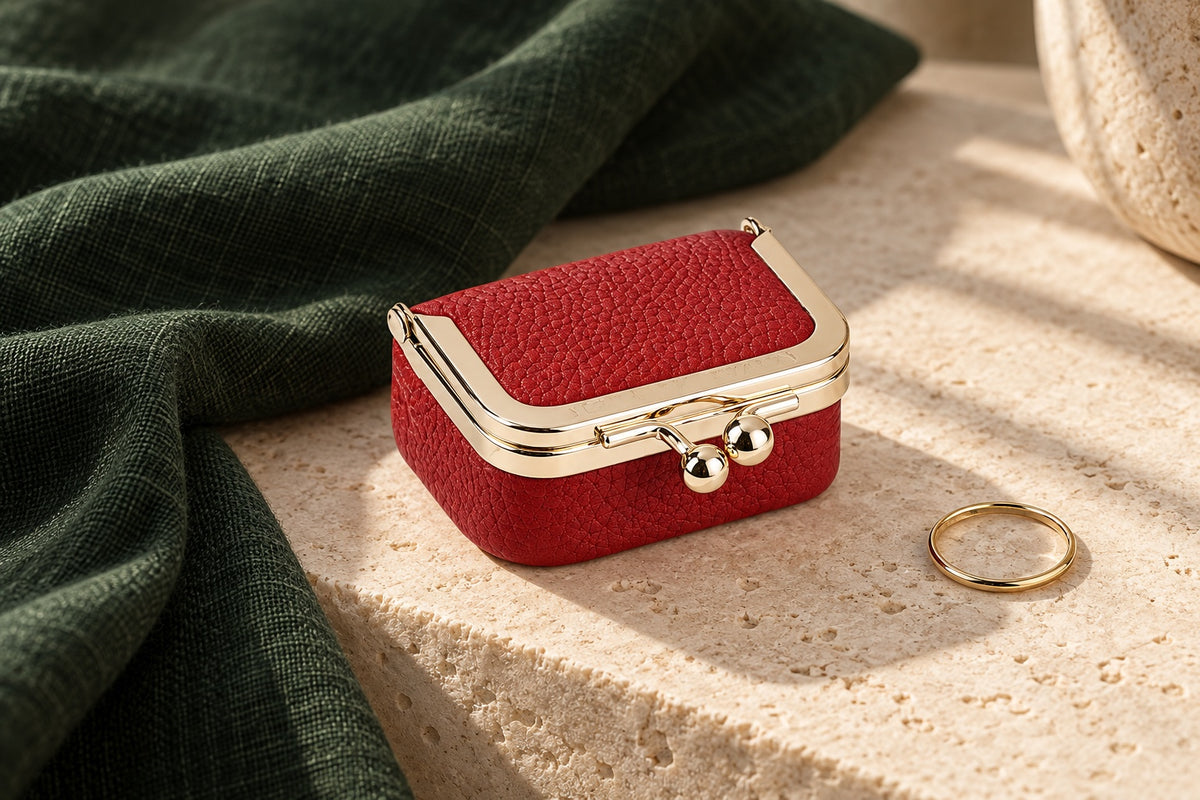 Red 1894 leather kiss-lock case with gold-tone clasp on warm limestone